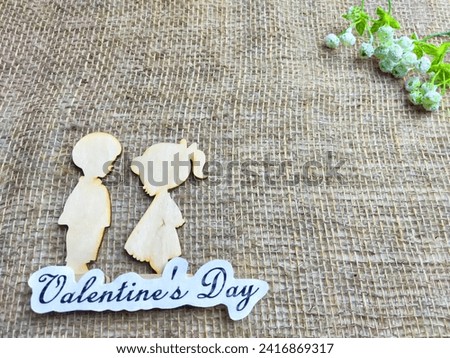 Wooden figurines of couple on jute background and inscription Valentine's Day. Concept of holiday. Card, Texture, Frame, copy space, place for text