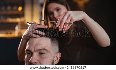 Young hairdresser female hands with scissors and comb hairstyle hairdressing close-up image in modern low light black style barber shop. Haircare service small business Cosmetics and personal care Royalty-Free Stock Photo #2416870517