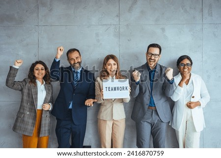 Portrait of multi ethnic successful business team looking at camera in the office and team leader holding sign ''teamwork'' in hands. Portrait of a group of businesspeople standing together  Royalty-Free Stock Photo #2416870759