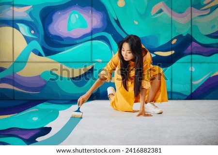 Female street artist painting colorful graffiti on the ground with copy space Modern art, urban concept. Royalty-Free Stock Photo #2416882381