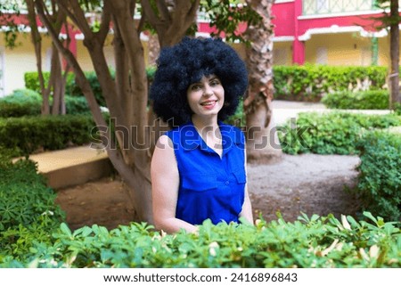 Portrait a woman with black curly hair and a beautiful smile in a blue dress.