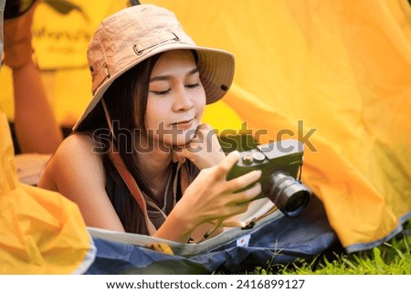 Young asian female tourist in safari dress and camera in her hands while lying inside the tent in the midst of nature in the morning,
