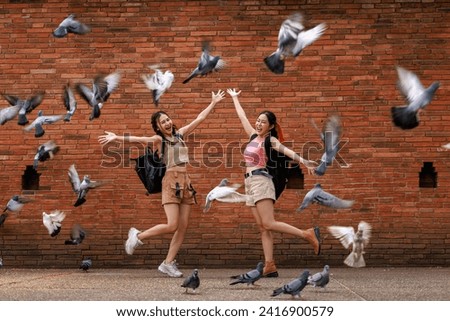two asian tourist girl happy standing posing and pointing hand while the pigons fly and eat at the tha phae gate, chiang mai thailand, travel destination concept,