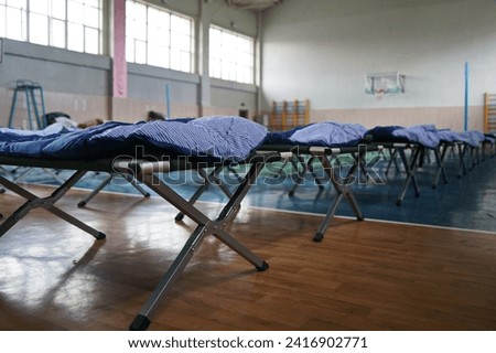 Cots with sleeping bags are placed in the school gym during an emergency Royalty-Free Stock Photo #2416902771
