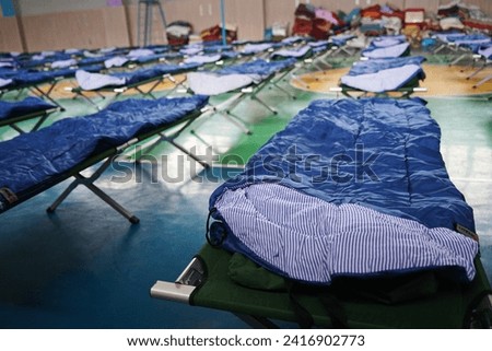 Cots with sleeping bags are placed in the school gym during an emergency Royalty-Free Stock Photo #2416902773