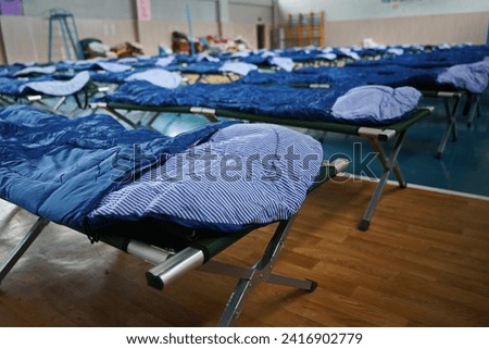 Cots with sleeping bags are placed in the school gym during an emergency Royalty-Free Stock Photo #2416902779