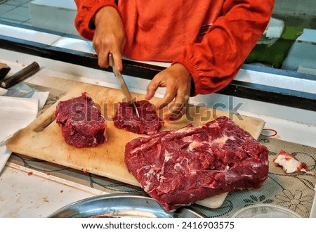 Picture of people cutting raw red beef meat and put on white cutting board in traditional market