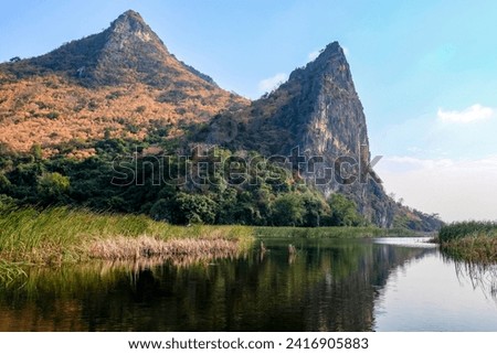 A stunning landscape photo of a lake with a mountain in the background. The lake is a deep blue color and is surrounded by lush green trees. The mountain is snow-capped and has a jagged peak. 