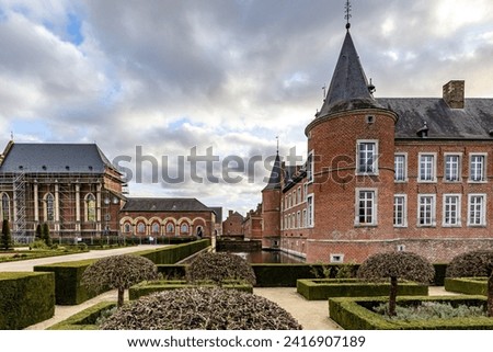 Exterior of  former 16th century Alden Biesen castle, garden with bushes and small trees, moat, buildings with windows and brick walls, one under renovation, cloudy day in Bilzen, Limburg, Belgium Royalty-Free Stock Photo #2416907189
