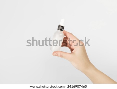 hand holding white serum in a glass bottle on a white background. skin care concept