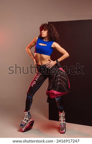 Curly woman in sportswear and bag wearing kangoo jumpers posing in studio on background