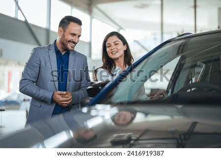 Couple at car dealership. Happy beautiful couple is choosing a new car at dealership. Happy young couple standing alongside their dream car and looking in