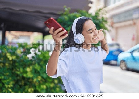 Young beautiful hispanic woman listening to music and dancing at street