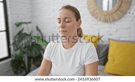 Beautiful, young blonde woman finds balance meditating with yoga exercises, breathing calmly, sitting on bed, engrossed in serenity amidst the cozy indoor atmosphere of her bedroom.