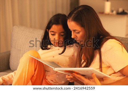 Mom and daughter reading a book on the couch before bedtime