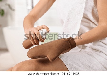 Self-tanning. Woman applying cosmetic product onto tanning mitt indoors, closeup Royalty-Free Stock Photo #2416944435