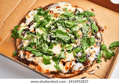 A fresh vegetarian pizza with arugula, cheese, and balsamic in a cardboard box.