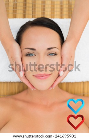Peaceful brunette enjoying a facial massage against hearts
