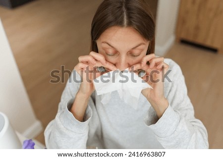 Allergy, flu, cold, rhinitis. Funny face of sick woman with paper tissues inside nose from runny nose and sneezes at home. Hay fever, sinusitis and female with viral infection blowing in handkerchief. Royalty-Free Stock Photo #2416963807
