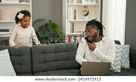 African american father and daughter sitting on sofa working while child disturb at home
