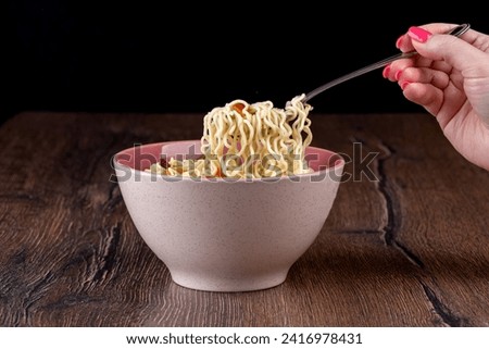 A woman's hand holds a fork with ready-made instant noodles. Copy space.