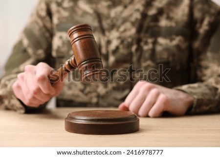 Law concept. Man in military uniform with gavel at wooden table, closeup