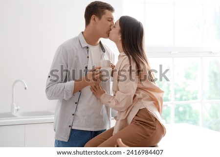 Happy young couple kissing in kitchen Royalty-Free Stock Photo #2416984407