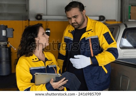 Professional Uniformed Car Mechanic Working in Service Station. Team Discussing and Repairing Vehicle. Checking List in The Automobile. Selective Focus