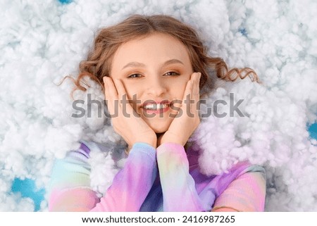 Young woman lying on white cloud against blue background, top view