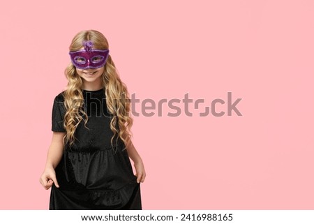 Happy little girl wearing carnival mask on pink background