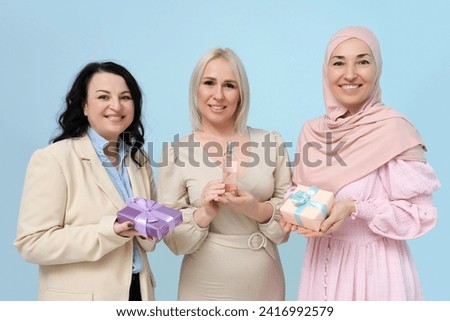 Mature women with gift boxes and perfume on blue background. International Women's Day