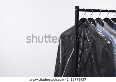 Dry-cleaning service. Many different clothes in plastic bags hanging on rack against white background, space for text Royalty-Free Stock Photo #2416996457