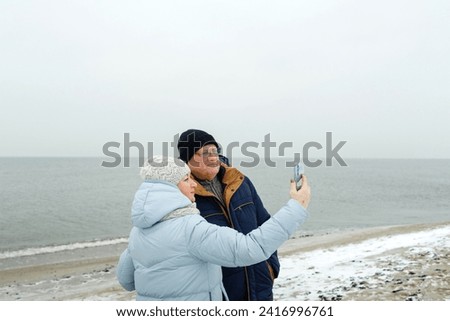 Portrait of an elderly couple enjoying a winter walk on the beach, taking a selfie.