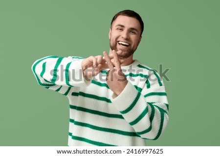 Handsome young man making hashtag sign with fingers on green background