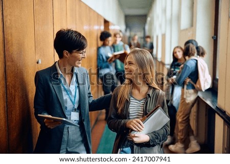 Happy high school teacher talking to her student while walking through the hallway. Royalty-Free Stock Photo #2417007941