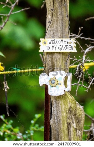 Welcome to my garden. Sign wood trunk post. Backyard yard patio. Blurred background bokeh. Spring springtime summer. Seasons. Green plants. Decor decoration. Welcoming.