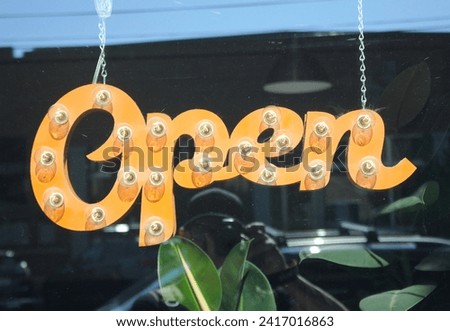 An open sign displayed on window side amidst lush green plants