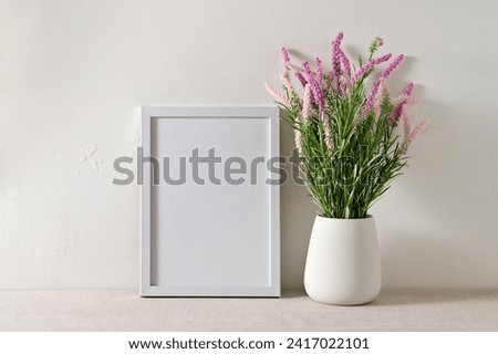 Aesthetic minimalist spring floral home interior decor, blank poster or picture frame mockup, pink flowers in vase on beige linen table cloth, plaster wall background with soft sunlight shadows.