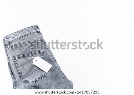Classic blue jeans with with empty tag on white background top view, copy space for your design. Fashion sale and promo banner. Shopping concept.