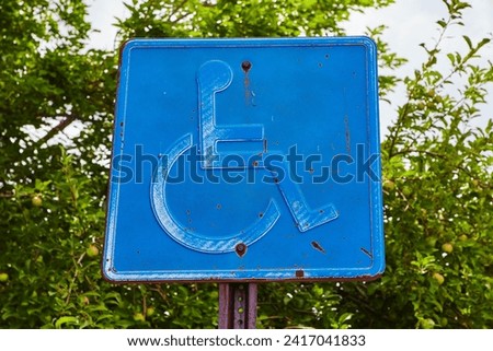 Weathered Handicap Parking Sign with Green Foliage Background
