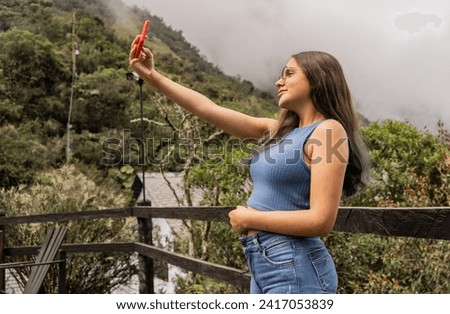 young woman with long hair walking outdoors in the park and taking a selfie with her mobile phone 
