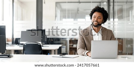 African-American young businessman working on his laptop in a contemporary office space with glass partitions on the backdrop. Concept of business and technology, bunner, panoramic view Royalty-Free Stock Photo #2417057661