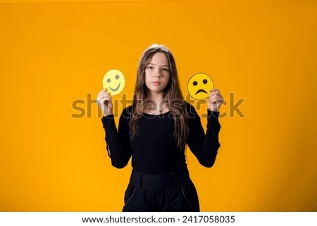 Upset girl holds emoticons with happy and sad emotions.