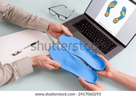 Female doctor orthopedist  presents new custom made insoles to a male patient in a clinic.  Feet recreation and orthotic medicine concept Royalty-Free Stock Photo #2417060293