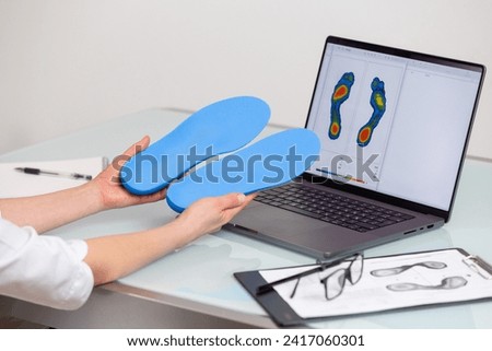 Female doctor orthopedist  holding custom made insoles in a clinic in front of the laptop with a test feet picture.  Feet recreation and orthotic medicine concept. Feet recreation medicine concept Royalty-Free Stock Photo #2417060301