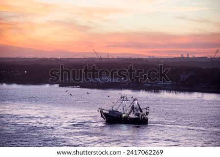 The sunset view of a fishing boat passing by along St. Johns River and Jacksonville downtown skyline in a background (Florida).