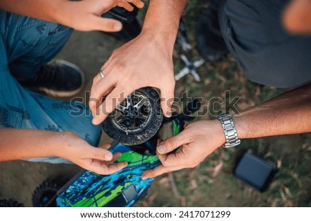 Cropped picture of hands repairing and changing tire on a broken remote control car during play and family time in nature. Hands fixing a malfunction on a broken toy car.