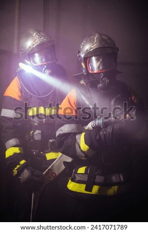 Portrait of firefighters in firefighting gear and helmet preparing to fight a fire. Dark background with smoke and blue light in a building on fire.