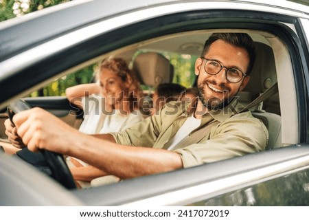 Portrait of a handsome smiling man driving a car. Father enjoying road trip on weekend and traveling by automobile with his family. Holiday and travel concept. Royalty-Free Stock Photo #2417072019