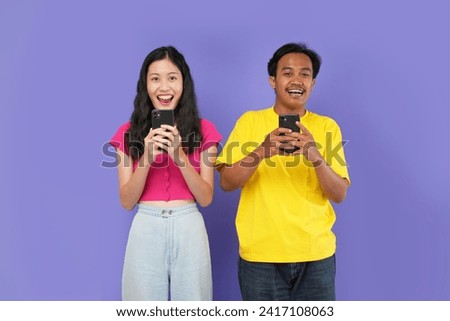 Young happy couple two friends family asian man woman wear casual clothes hold in hand use mobile cell phone together surfing internet isolated on purple color background studio portrait